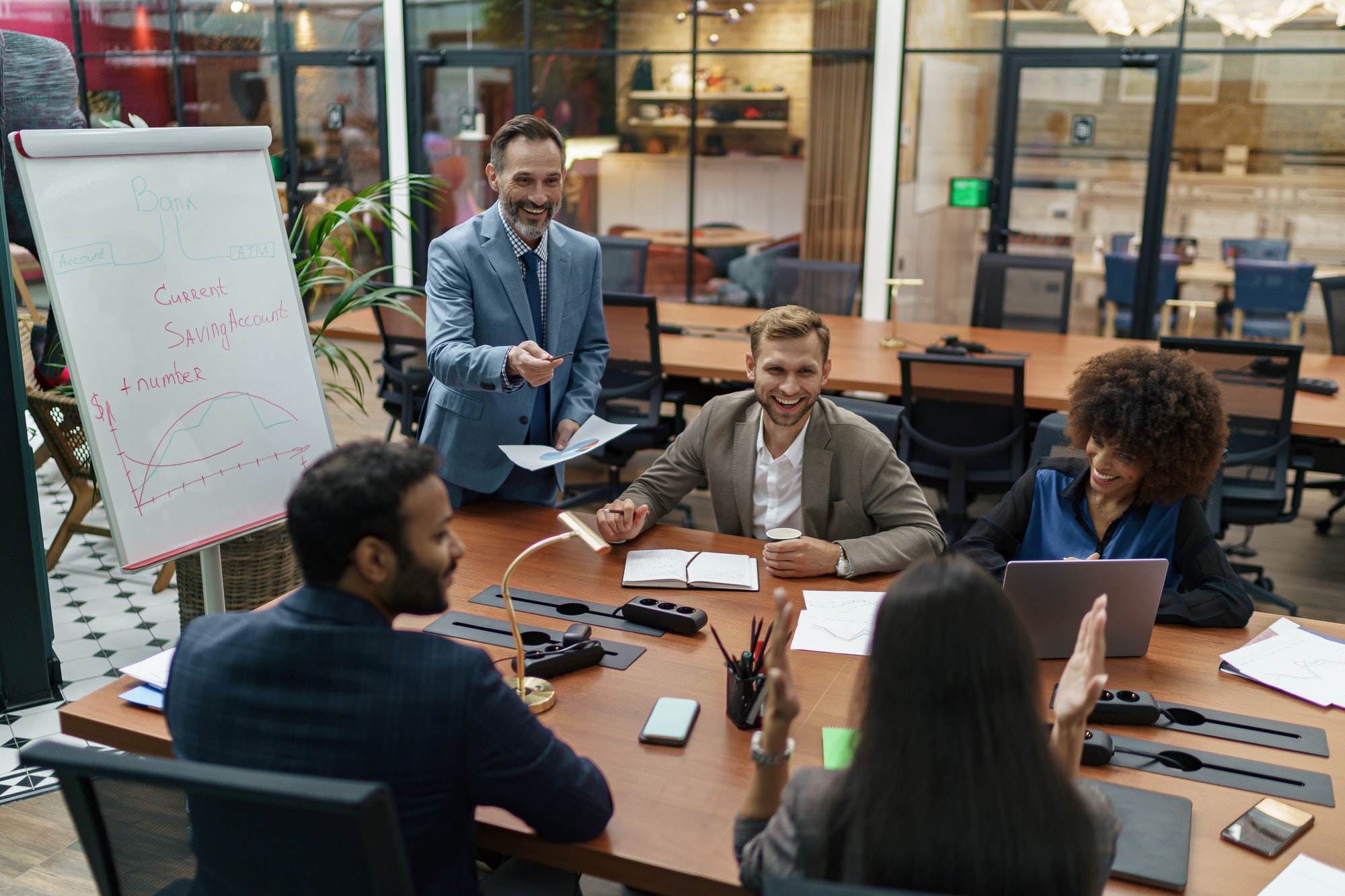 Mature business coach or speaker make flip chart presentation to diverse businesspeople at meeting